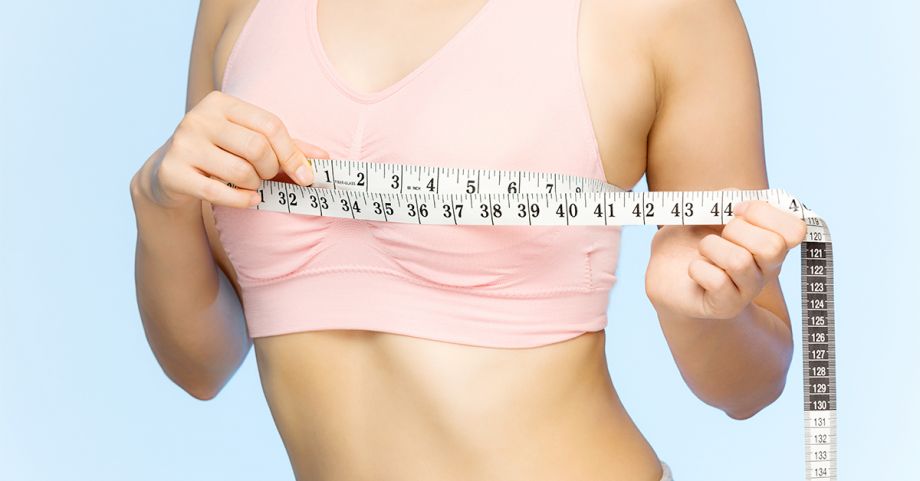 small young woman holding a tape measure to her breasts, regarding value of breast reduction